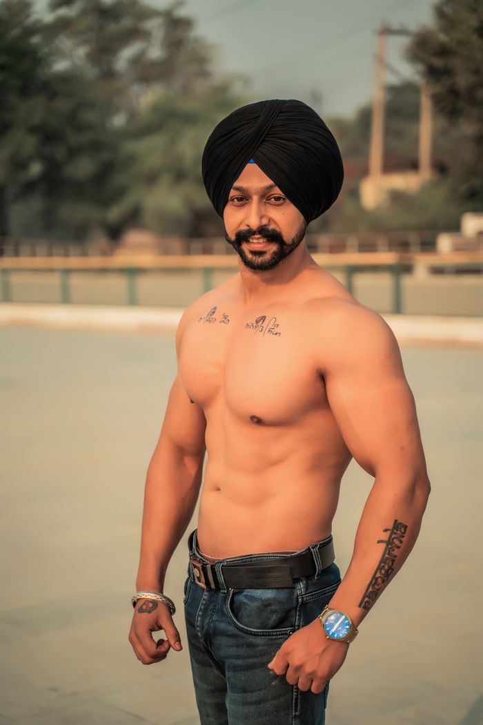 Fit shirtless man with a turban posing outdoors, showcasing muscular physique.